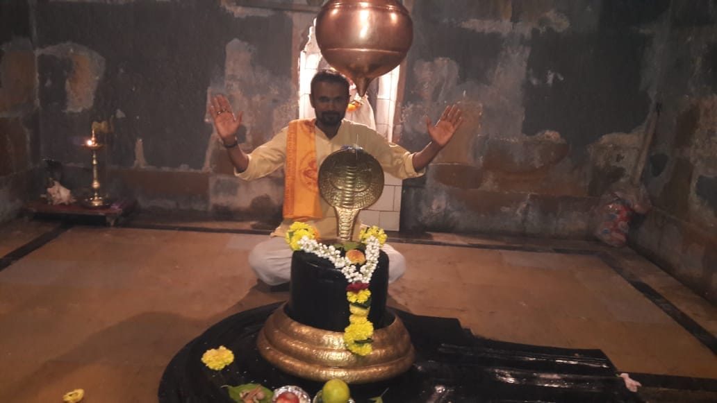 Priest in prayer before a Shivling with a nag hood in a temple