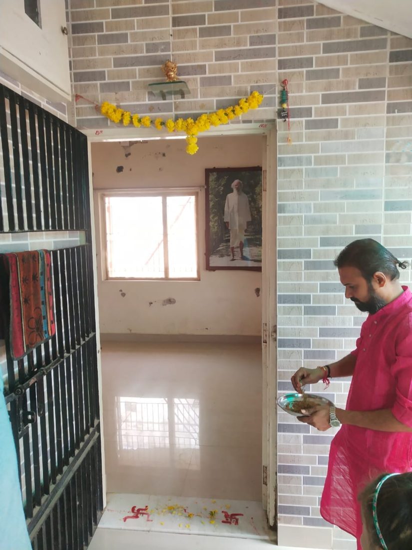 Priest performing a puja at a home entrance with a marigold toran and swastik marks