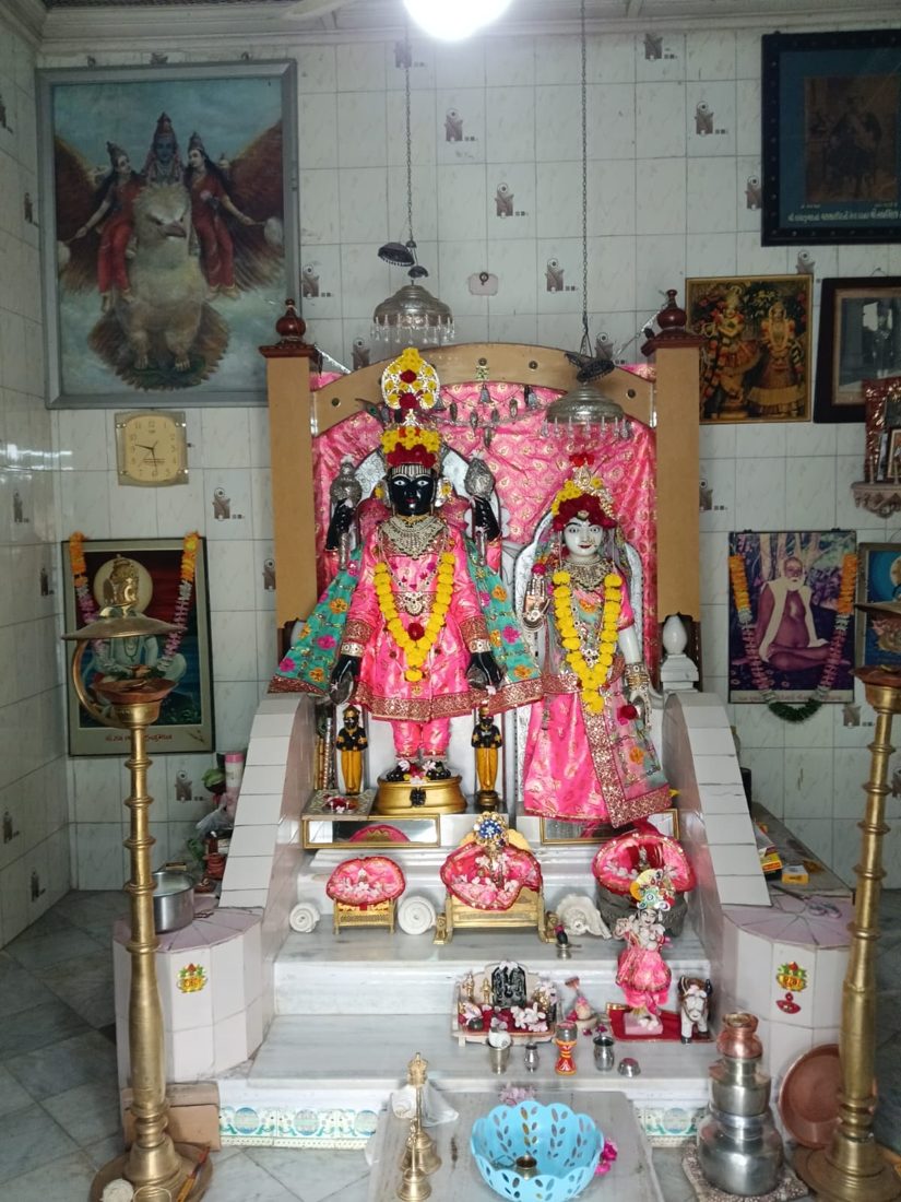 Temple shrine with a pair of decorated deity idols in pink attire, marigold garlands and tall brass lamps